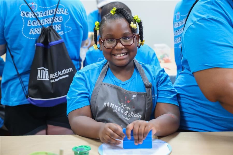  A girl smiles to the camera while working on an art project.